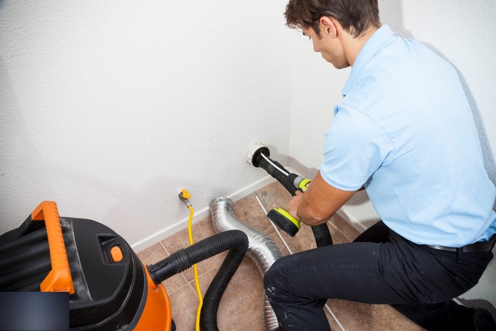 Technician cleaning a residential dryer vent duct with a vacuum and rotary brush system.