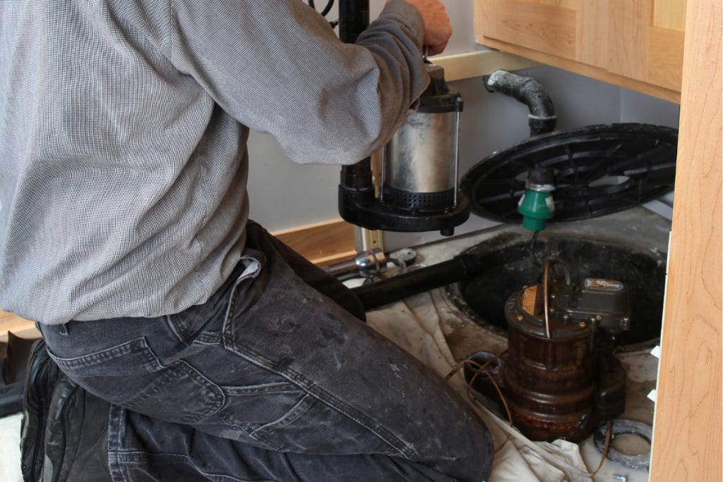 Technician replacing a sump pump inside a basement sump pit.