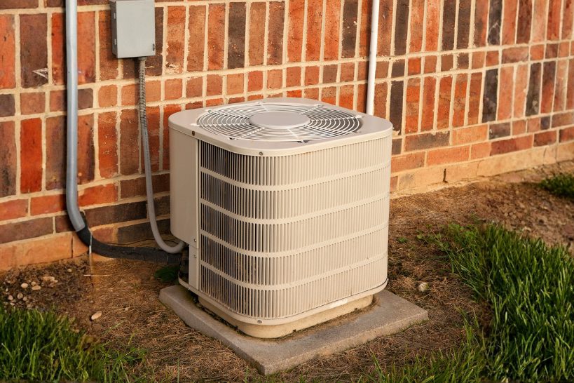 Outdoor HVAC unit beside a brick home, ready for winter clearing and seasonal maintenance.