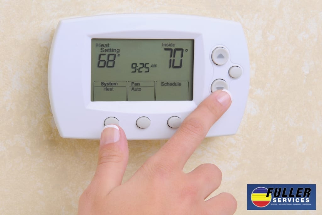 Hand adjusting a home thermostat to set a comfortable indoor heating temperature.
